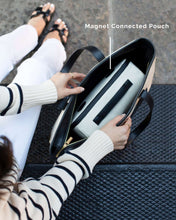 Person opening a black and white canvas magnet-connected pouch on a textured surface. 