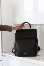 Woman's hand grabbing the top handle of a black smooth vegan leather insulated lunch and laptop backpack.
