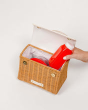 Open view of the Natural Wicker Oyster Mini by Modern Picnic showing the insulated interior, with a hand placing a red juice bottle beside a food container.