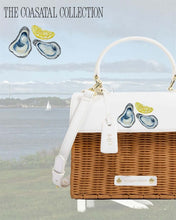 The Natural Wicker Oyster Mini by Modern Picnic featured in a coastal setting with oysters and lemon artwork, sailboats, and shoreline scenery promoting the Coastal Collection.