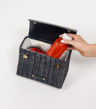 Open black wicker mini lunch bag with vegan leather flap showing insulated interior, holding a red juice bottle and bowl of raspberries – stylish and functional cooler bag by Modern Picnic.