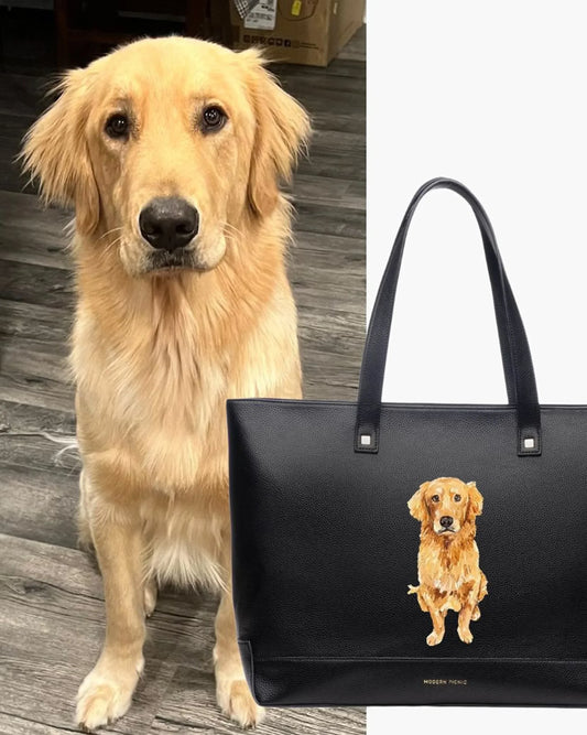 Golden retriever on wood floor beside black tote bag with golden retriever illustration