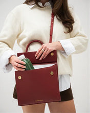 A woman in a cream sweater and white shirt holds open the red smooth lunch bag, revealing the insulated white interior as she places a green drink bottle inside, illustrating the bag's capacity for beverages.