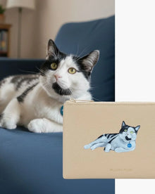 Beige vegan leather pouch with embroidered cat, matching real cat on blue couch
