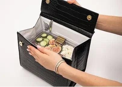Stylish black insulated lunch bag with vegan leather texture, holding fresh food like cucumbers and figs.