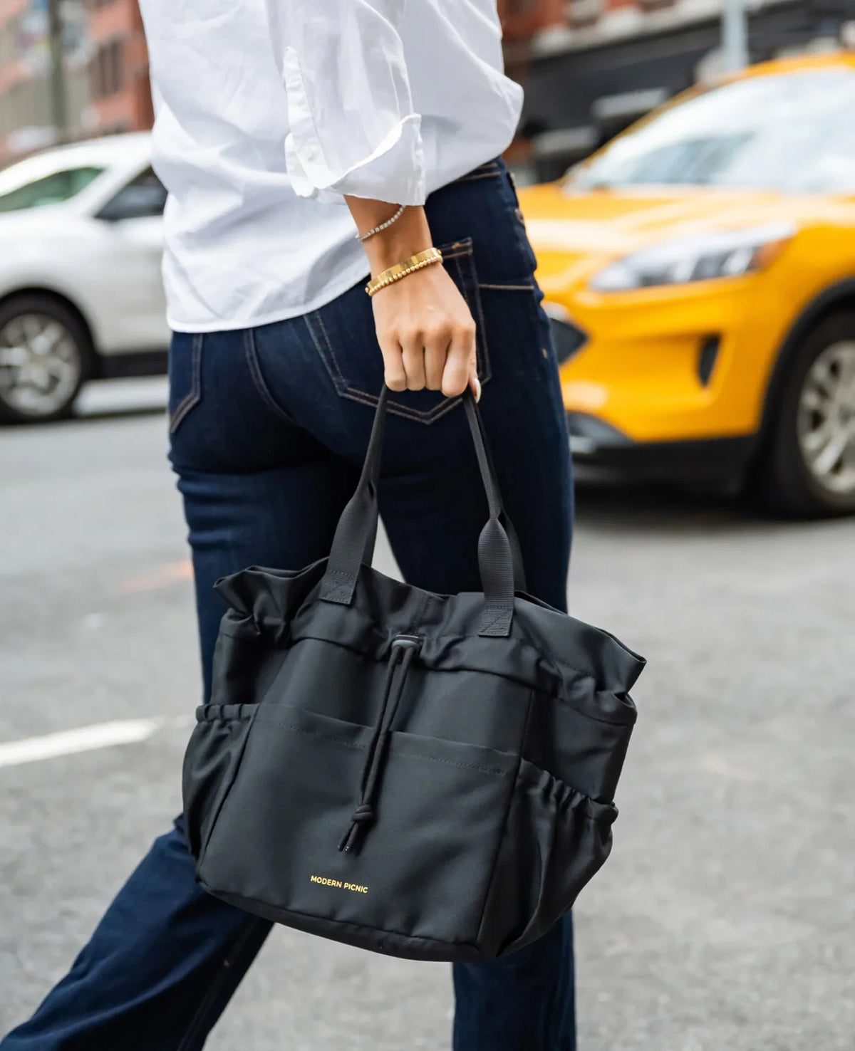 Person carrying a black Modern Picnic insulated lunch tote bag on a city street.