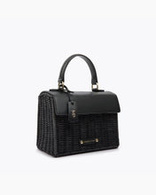 Angled view of a Modern Picnic black wicker mini top-handle bag with a leather flap and gold 'MP' tag and gold embosses "Modern Picnic" detailing at the bottom.