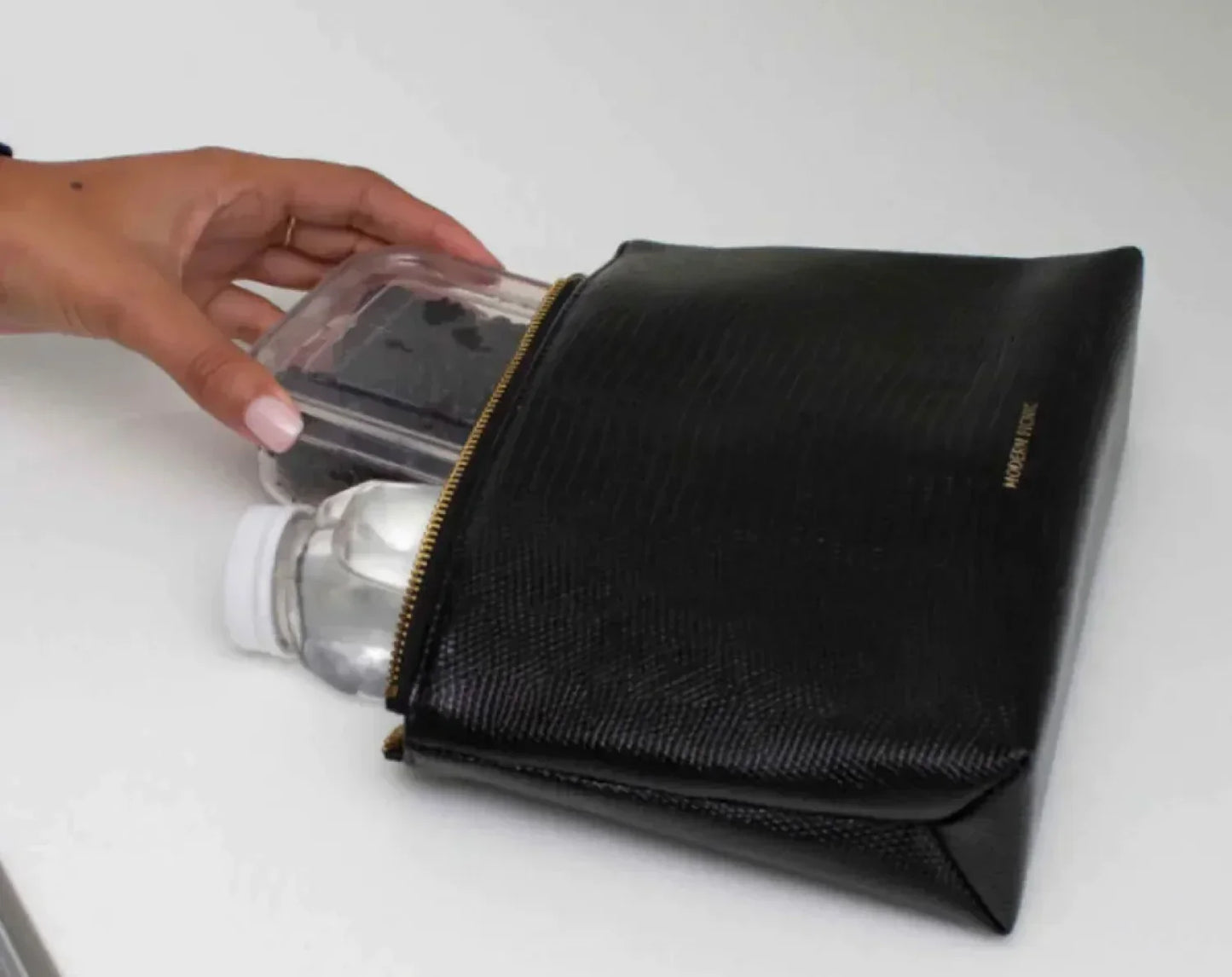 Hand placing a food container and water bottle into a black croc vegan leather lunch pouch