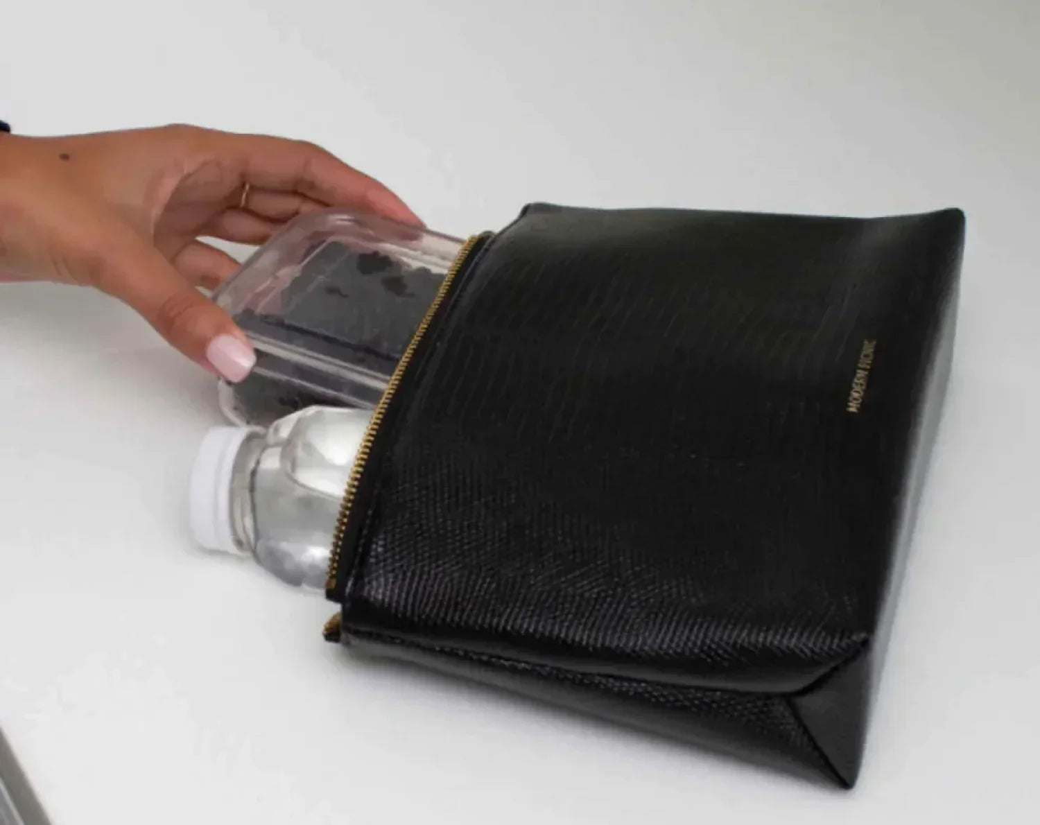 Hand placing a food container and water bottle into a black croc vegan leather lunch pouch