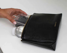 Hand placing a food container and water bottle into a black croc vegan leather lunch pouch