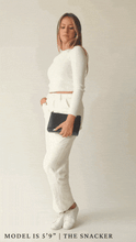 A full-body animation shows a blonde woman wearing a white long-sleeve top and white trousers modeling the small, rectangular pouch.