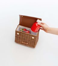 Open view of The Wicker Mini in Brown Wicker Lobster by Modern Picnic showing the insulated interior, with a hand placing a red juice bottle beside fresh strawberries.