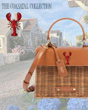 The Wicker Mini in Brown Wicker Lobster by Modern Picnic showcased in a coastal setting with Nantucket-style homes and hydrangeas, promoting the Coastal Collection.