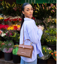 Woman wearing a light blue shirt and jeans carrying The Wicker Mini in Brown Wicker Lobster by Modern Picnic as a crossbody while shopping at a flower market.