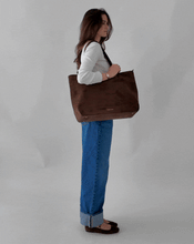 Short video clip of a female model wearing a white long-sleeve shirt and wide-leg denim jeans, confidently posing and walking while carrying a dark brown suede tote bag.