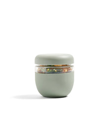 Sage green airtight food storage container with clear middle, filled with salad, on white background.