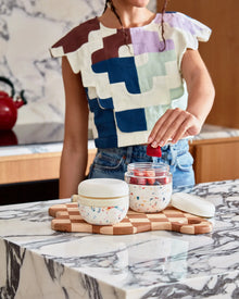 Woman in kitchen placing fruit in terrazzo print insulated food container on marble counter.