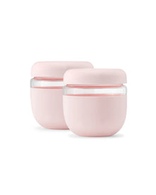 Set of two blush pink, seal-tight glass food containers with rounded lids on white background.