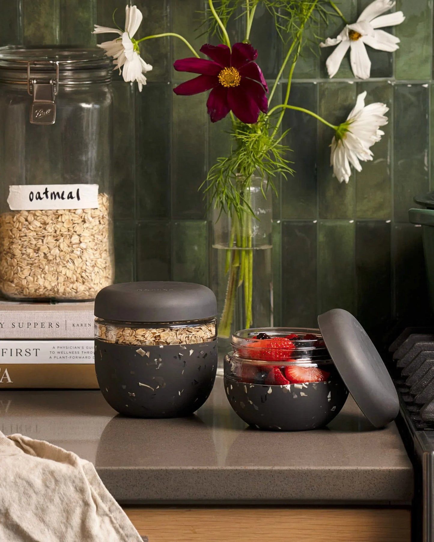 Charcoal terrazzo seal-tight lunch bowls on a kitchen counter, one filled with oats and the other with fresh berries.