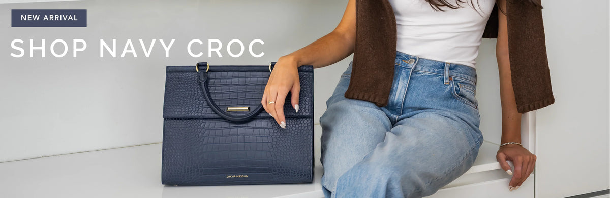 Navy blue croc-embossed vegan leather insulated lunch bag next to a person in jeans.