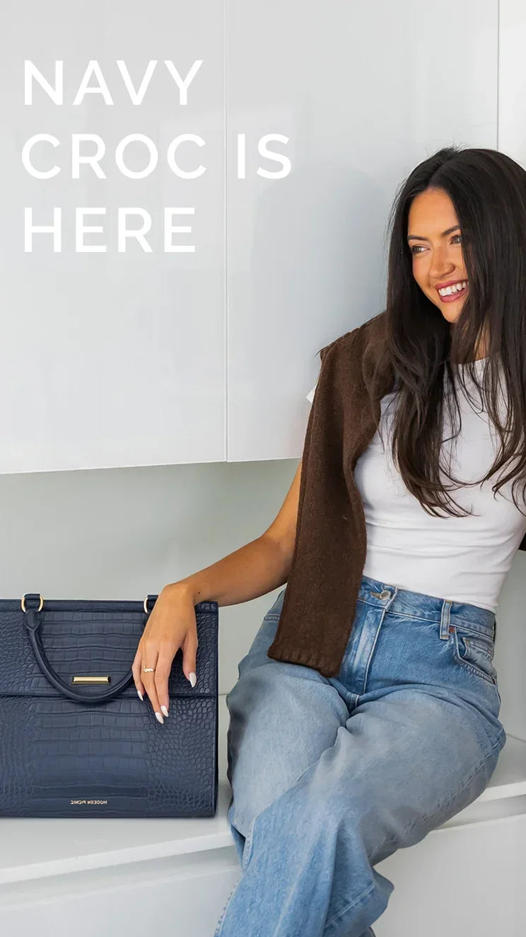Woman sitting next to a navy blue croc-embossed vegan leather tote bag.