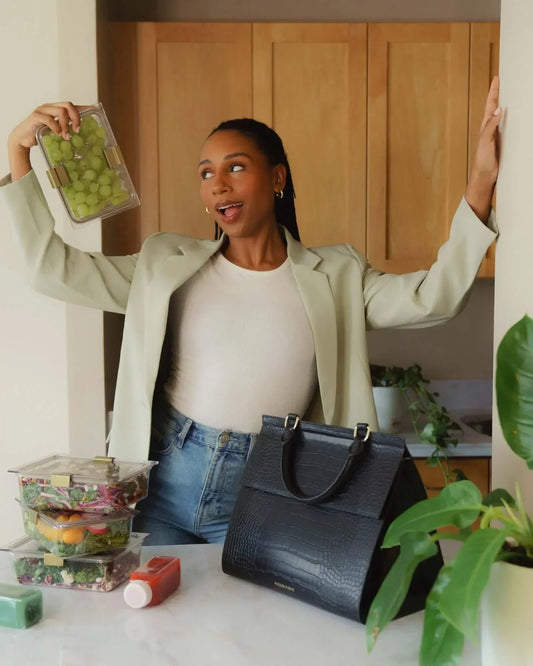 Woman in kitchen holding reusable food containers next to black large luncher bag