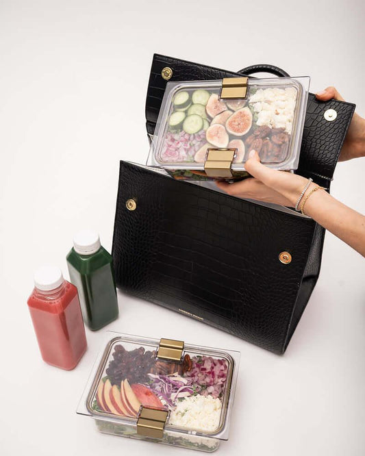 Chic black textured lunch tote with gold hardware holding healthy meal prep containers and juice bottles