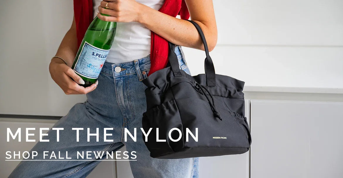 Woman holding a green glass bottle and a black nylon tote bag in casual denim jeans.