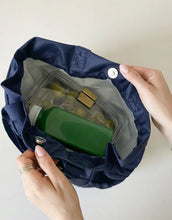 Top view of a navy insulated lunch bag with a green juice bottle and salad container inside.