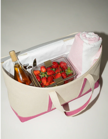 Canvas tote bag with pink accents, containing a drink, strawberries, and a towel.