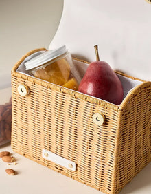 Insulated wicker-style lunch bag with jar of fruit and red pear inside, almonds nearby