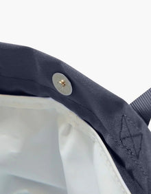 Close-up of navy lunch bag with gold snap button and white insulated interior, chic vegan leather design