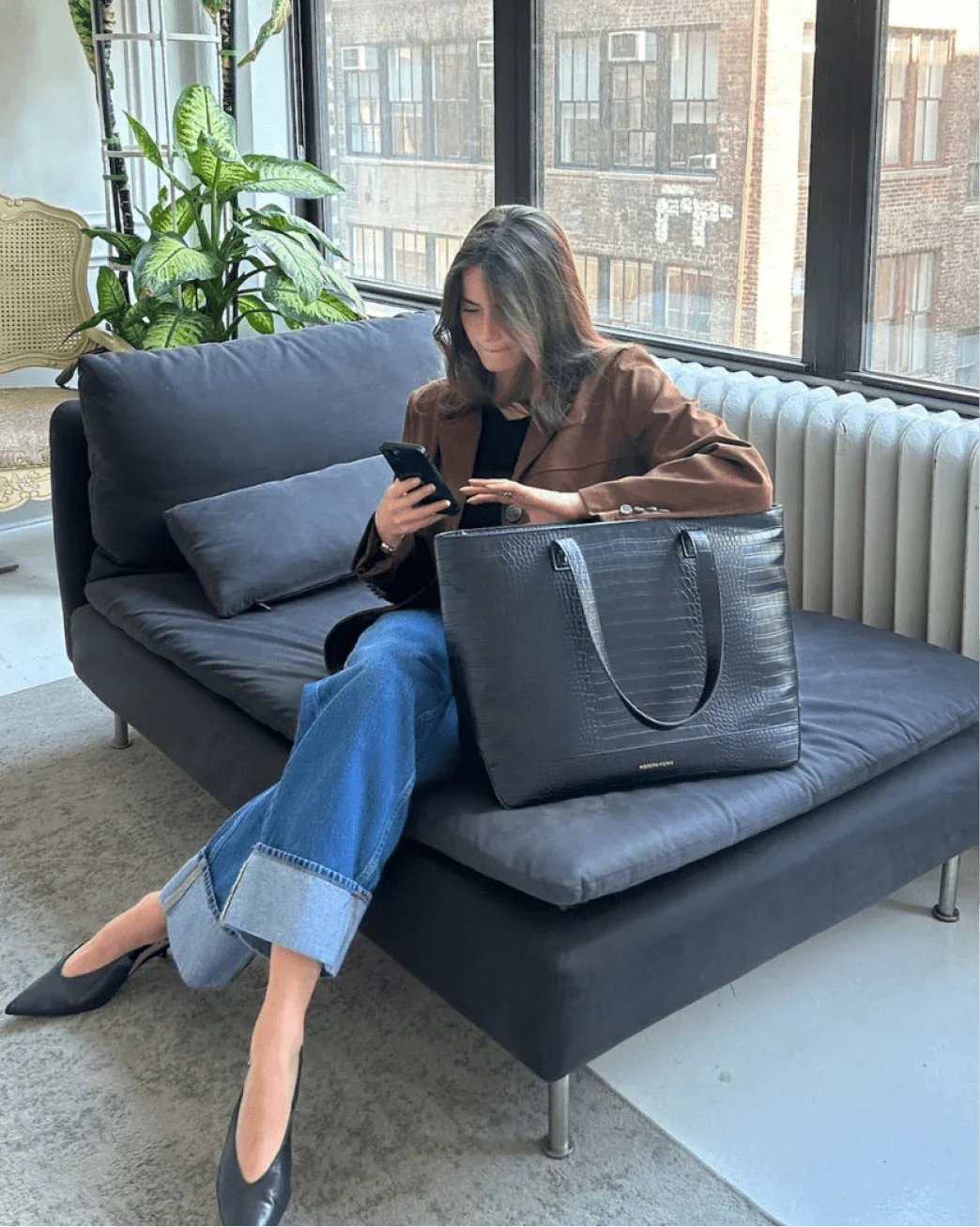 Woman sitting on sofa using Modern Picnic black croc tote bag while working on laptop