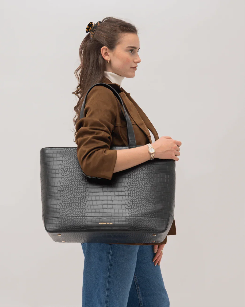 Side profile of woman carrying Modern Picnic black croc tote bag with brown jacket and jeans