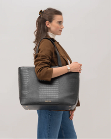 Side profile of woman carrying Modern Picnic black croc tote bag with brown jacket and jeans