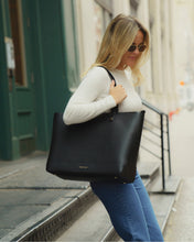 Woman carrying Modern Picnic black pebble tote bag over shoulder while walking in city