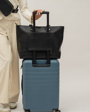 Modern Picnic black pebble tote bag secured on luggage handle, ideal for travel