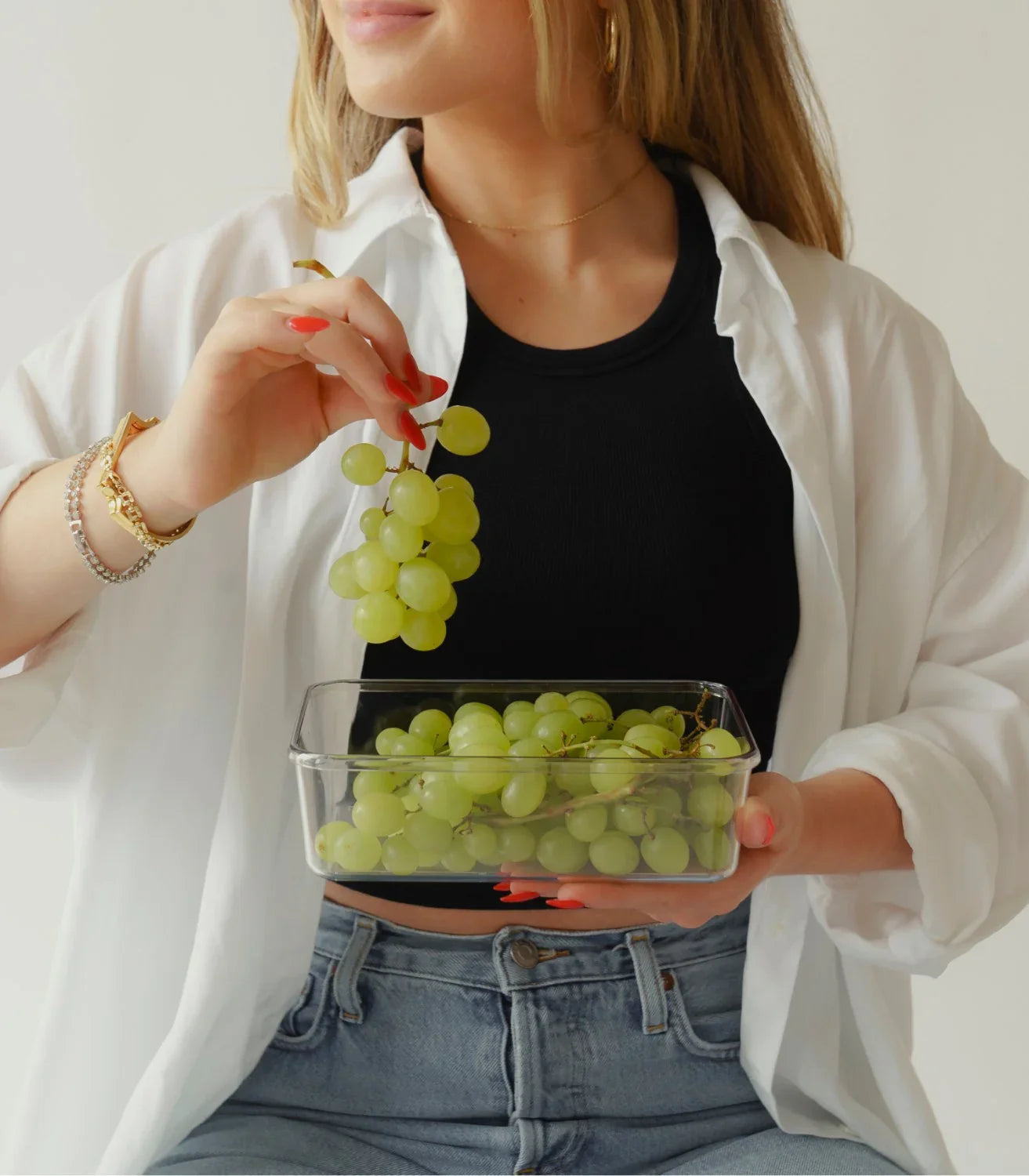 Woman in casual outfit holding a Modern Picnic container of grapes, illustrating the lunch set in use.