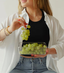 Woman in casual outfit holding a Modern Picnic container of grapes, illustrating the lunch set in use.