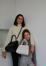 Mother and daughter standing side by side with matching Modern Picnic Mommy and Me Set bags in black and cream.