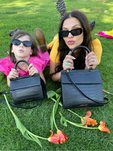 Mother and daughter relaxing on the grass with their matching Modern Picnic Mommy and Me Set bags and flowers nearby.