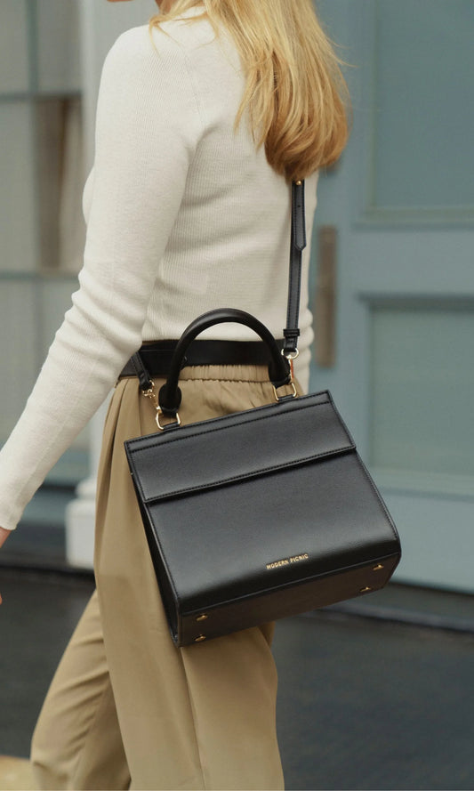 Woman wearing the Modern Picnic black handbag from THE DAY TO NIGHT SET over her shoulder, demonstrating versatile day-to-night use.