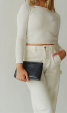 Woman holding the Modern Picnic black pouch from THE SNACKER SET while wearing neutral outfit, showing clutch-style versatility