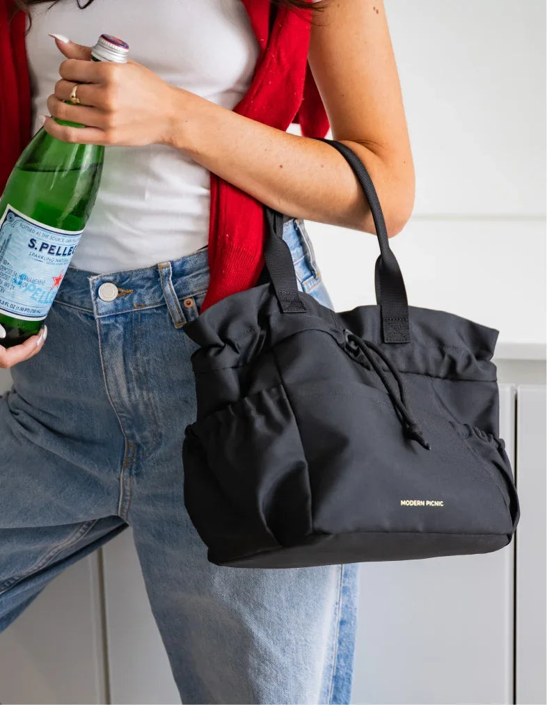 Woman in blue jeans and red cardigan carrying a black Modern Picnic insulated tote bag