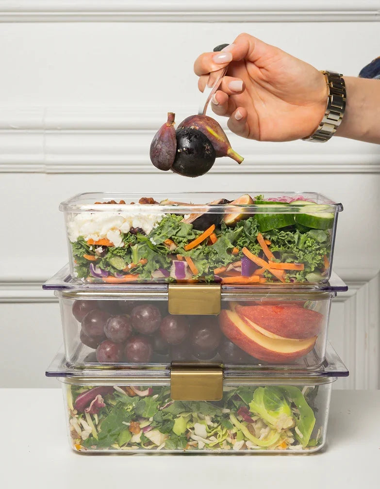 Stacked clear food storage containers filled with fresh salad, grapes, and sliced apples.
