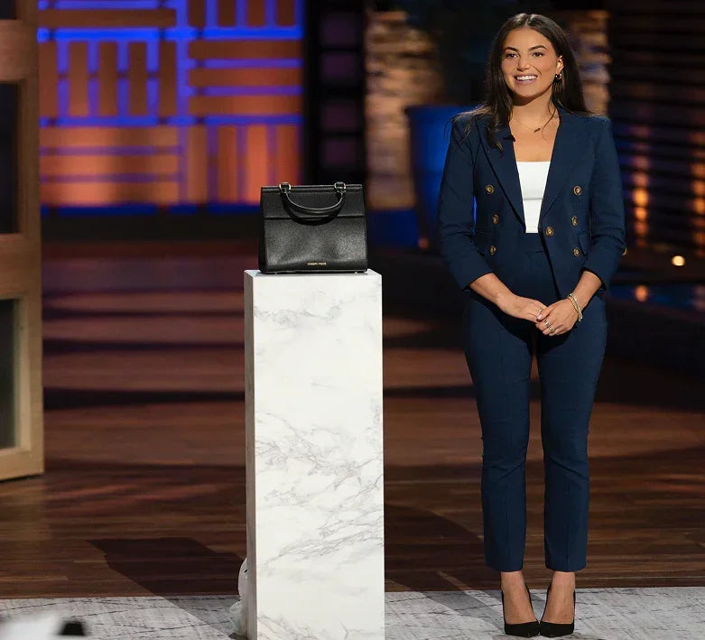 Stylish woman in navy suit beside black vegan leather handbag on marble pedestal, ideal for professional settings.