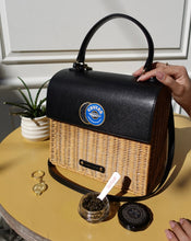 Black handbag with wicker design held by a hand on a table with a plant and container of the caviar co caviar