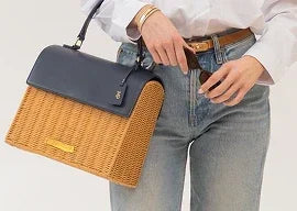 Woman wearing light blue jeans and white shirt carrying a woven straw tote with a navy blue flap.