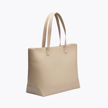 A three-quarter studio shot of a structured, large cream tote bag made of vegan leather. The bag has two tall shoulder straps and subtle gold hardware.