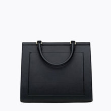 A back-facing studio shot of a structured large black handbag with a curved top handle. The back panel features a stitched-in slip pocket and is made of pebbled vegan leather.
